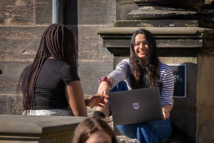 Two female students sitting in the cloister with laptops
